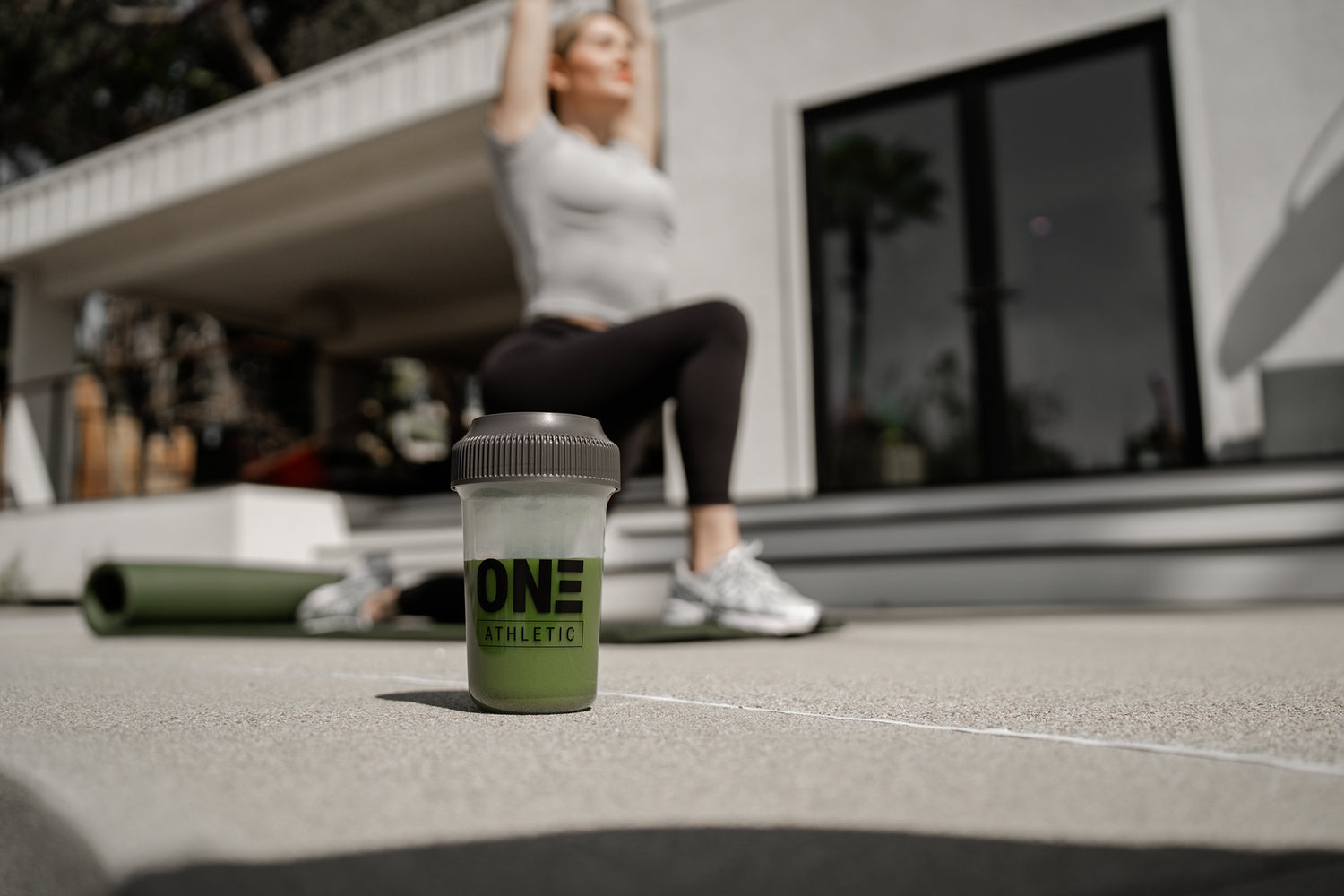 Woman Doing Lunges Behind Bottle of ON3 Athletic shaker