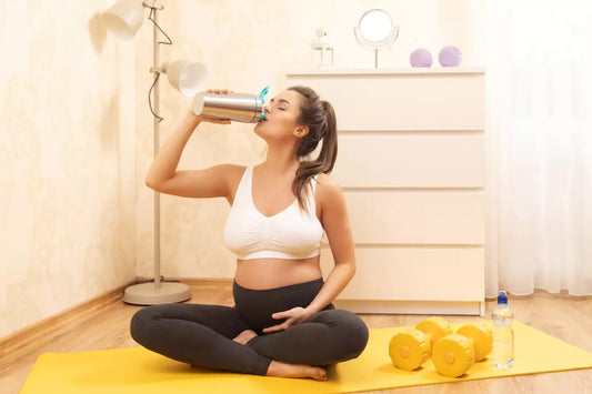 A pregnant woman in a home gym drinking a protein shake