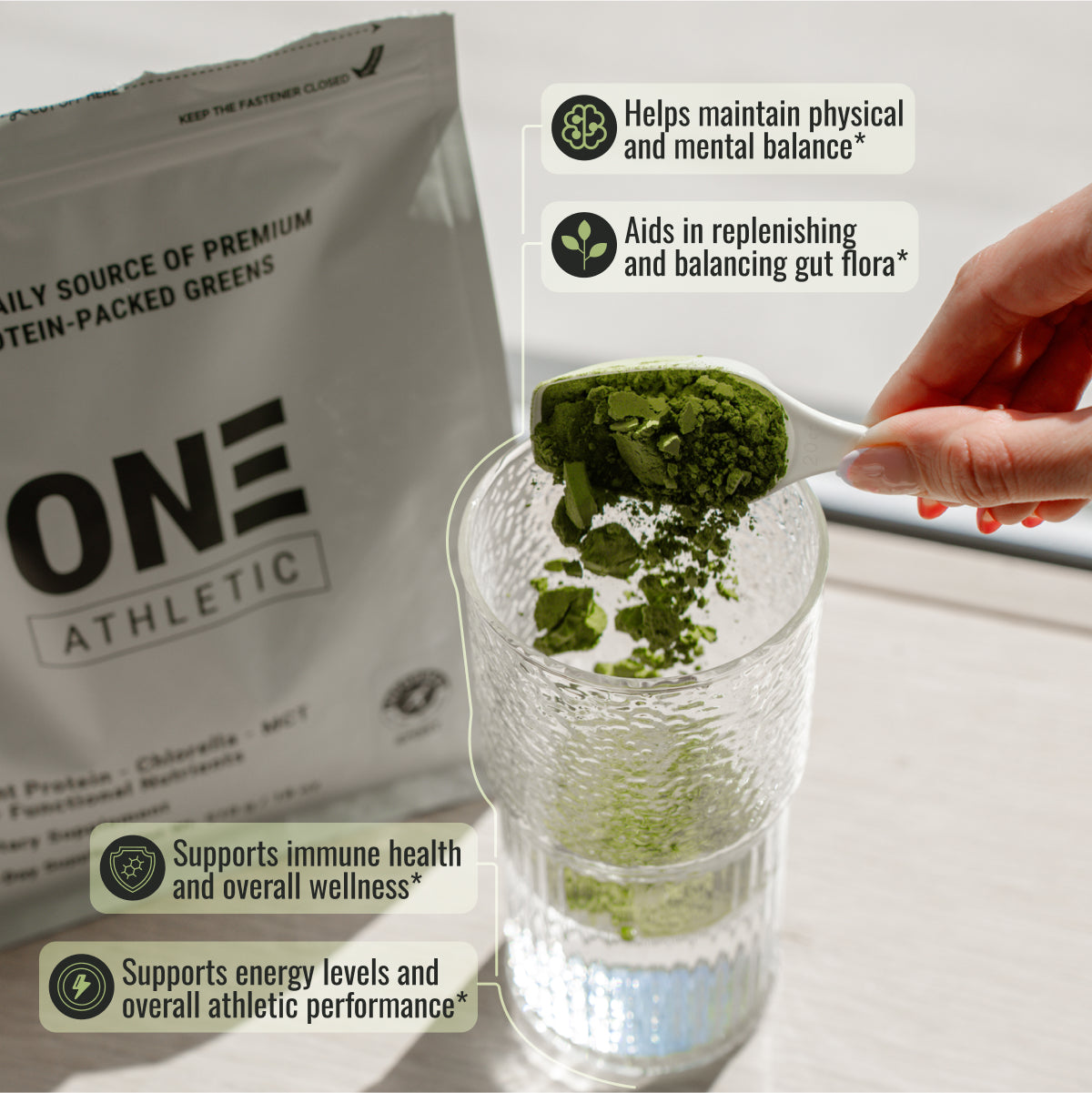 Green powder being added to a glass with One Athletic packaging in the background
